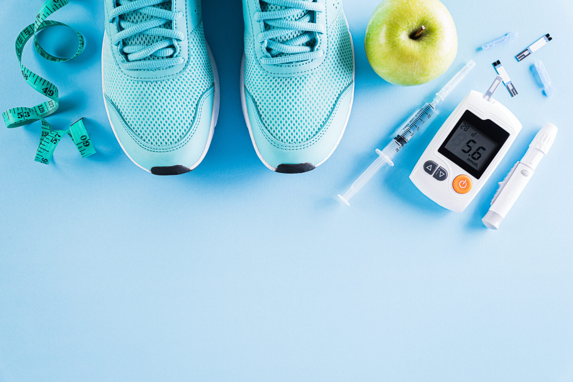 Top view of diabetes tester set with athlete's equipment; measuring tape, green dumbbell and  fruit on bright blue pastel background. Healthy lifestyle, food and sport concept.